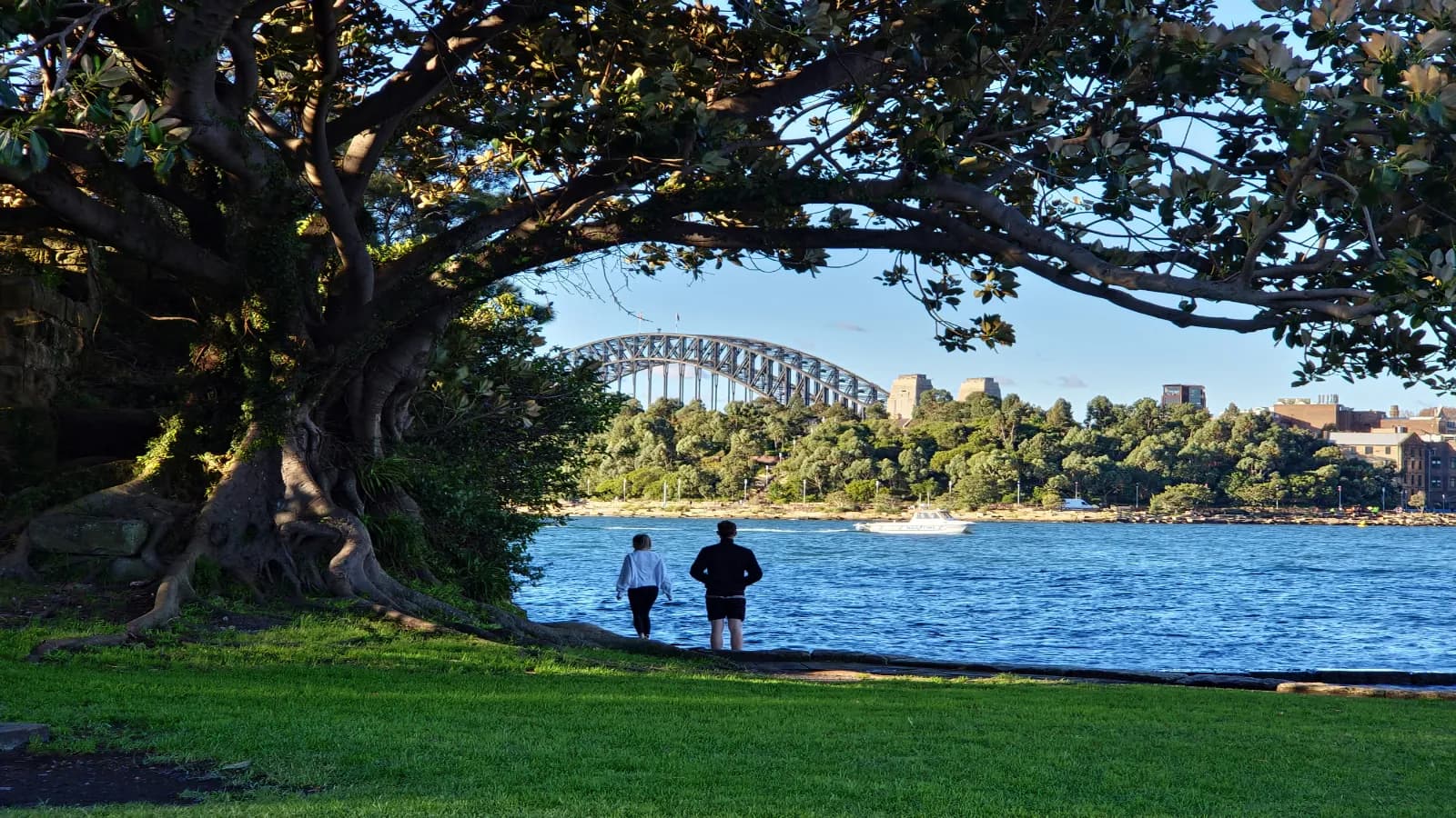 Couple walking beside Sydney Harbour in Balmain with the Harbour Bridge in the distance